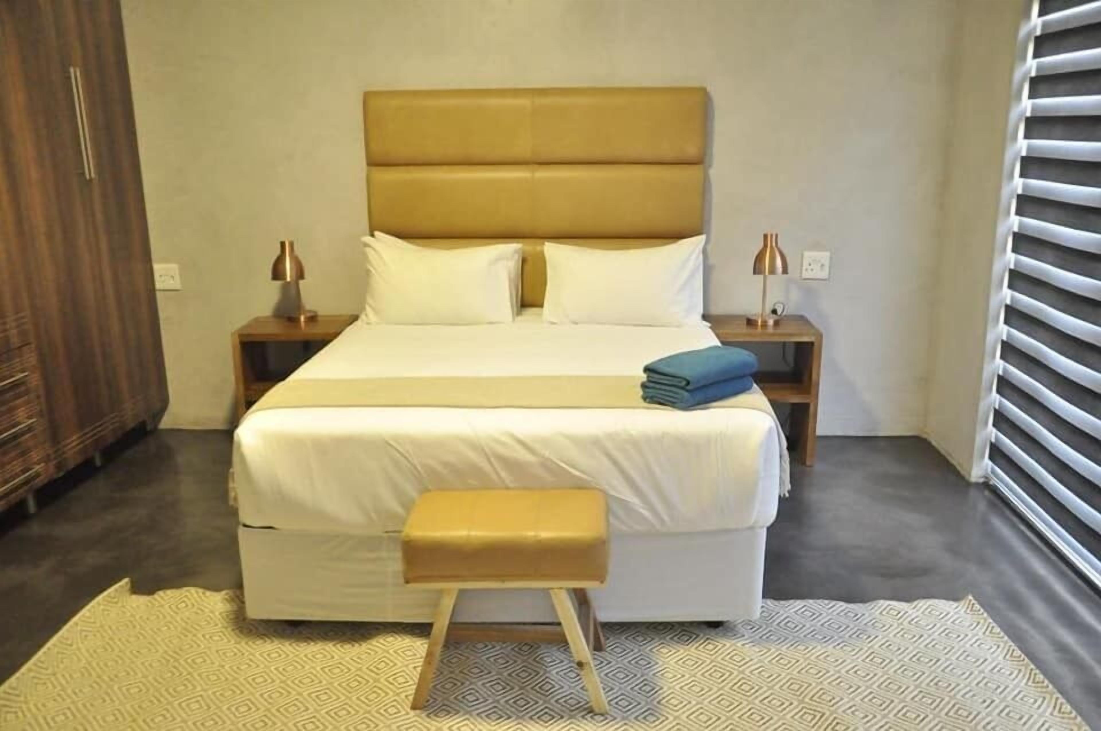 Ein Schlafzimmer mit einem großen Bett, zwei Nachttischen, einer Bank und einem Fenster mit Jalousien.