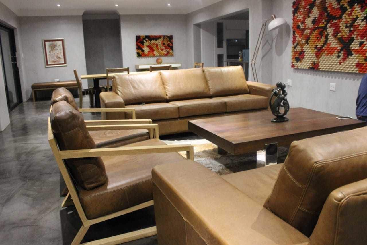 A modern living room with leather sofas and armchairs, a wooden coffee table, and a dining area with a bench and table.