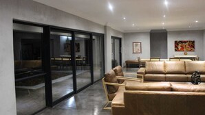 Een moderne woonkamer met een leren bank, een eethoek met een tafel en stoelen, en grote glazen deuren die leiden naar een buitenruimte.