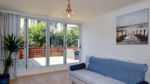 A modern living room with a white sofa, a large sliding glass door leading to an outdoor area, a potted plant, and a painting on the wall. - Cooleens- Chic 1-bedroom Apt. in North Berwick (North Berwick)