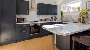 A modern kitchen with dark cabinetry, a large marble island, and a built-in oven. - Cooleens- Chic 1-bedroom Apt. in North Berwick (North Berwick)
