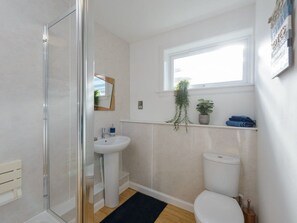 A modern bathroom with a glass shower enclosure, a pedestal sink, a toilet, and a window with a plant. - Cooleens- Chic 1-bedroom Apt. in North Berwick (North Berwick)