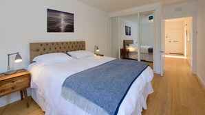 A bedroom with a large bed, a nightstand, a lamp, a blue ceiling light, a framed picture on the wall, and a door leading to another room. - Cooleens- Chic 1-bedroom Apt. in North Berwick (North Berwick)