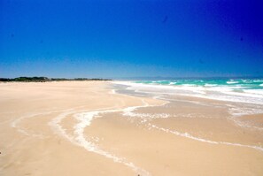 A wide sandy beach with gentle waves and a clear blue sky. - Beachfront Villa Africa Queen Jeffreys (Jeffreys Bay)
