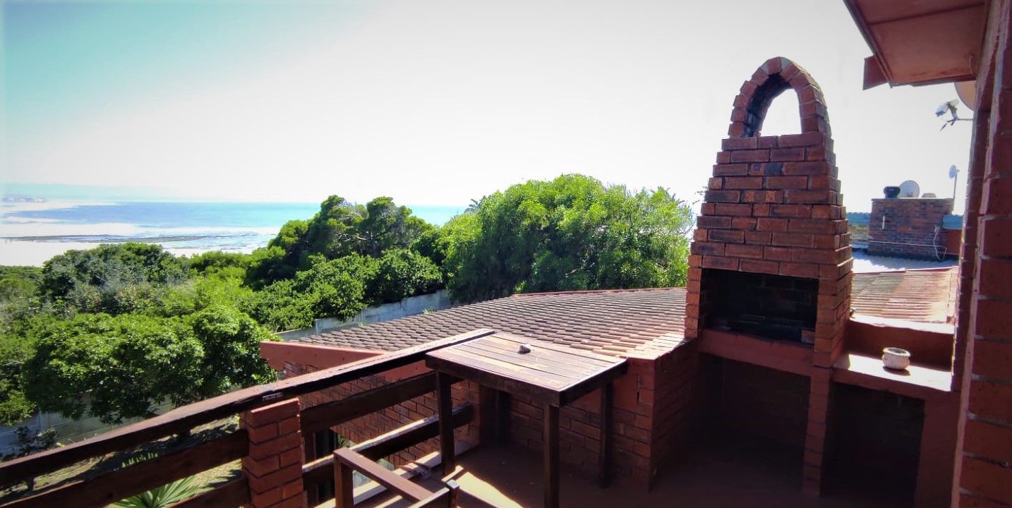 An outdoor barbecue area with a brick oven, a wooden table, and a view of the ocean.