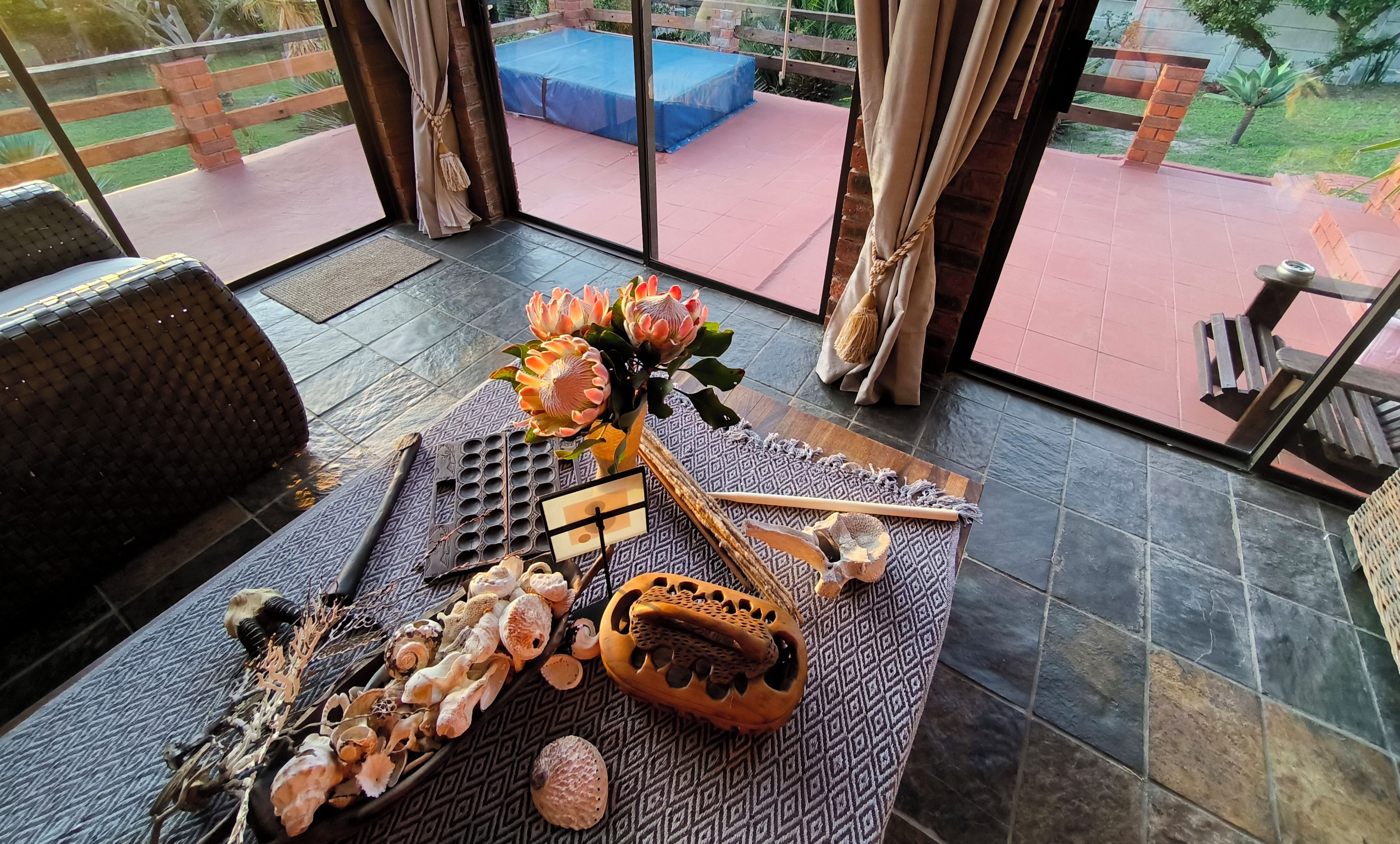 Une pièce dotée d’un sol à motifs, d’un canapé, d’une table agrémentée d’objets décoratifs, et offrant une vue sur un espace extérieur avec un tapis bleu et un mur en briques.