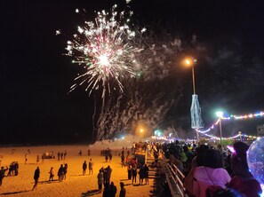 Une scène de plage avec des feux d’artifice, une foule et une structure illuminée de façon éclatante.