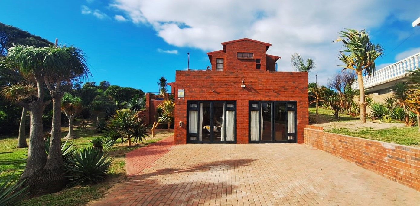 A modern brick building with large glass doors, surrounded by a landscaped garden with palm trees.