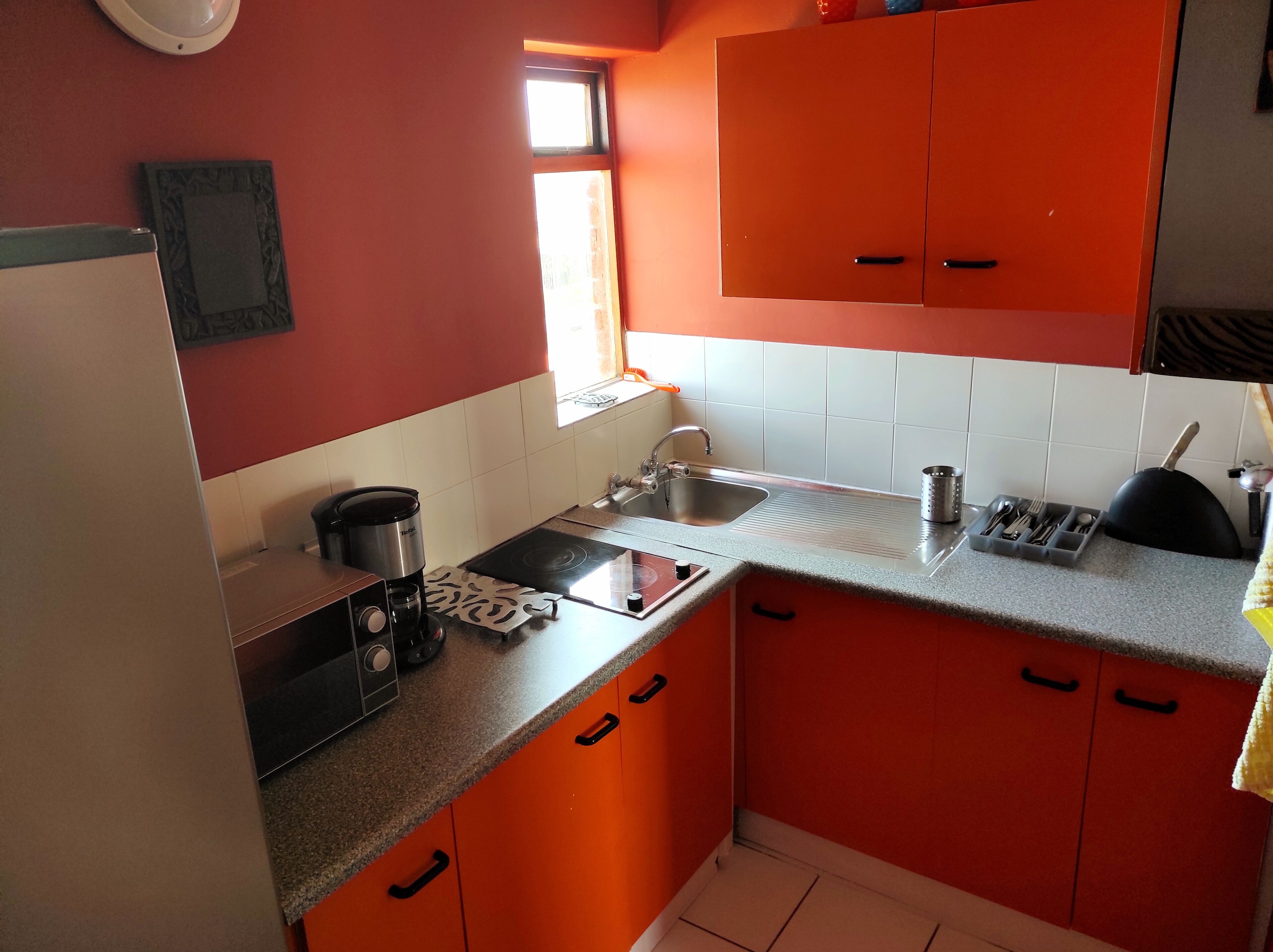Una cocina con armarios naranjas, estufa, pileta y ventana.