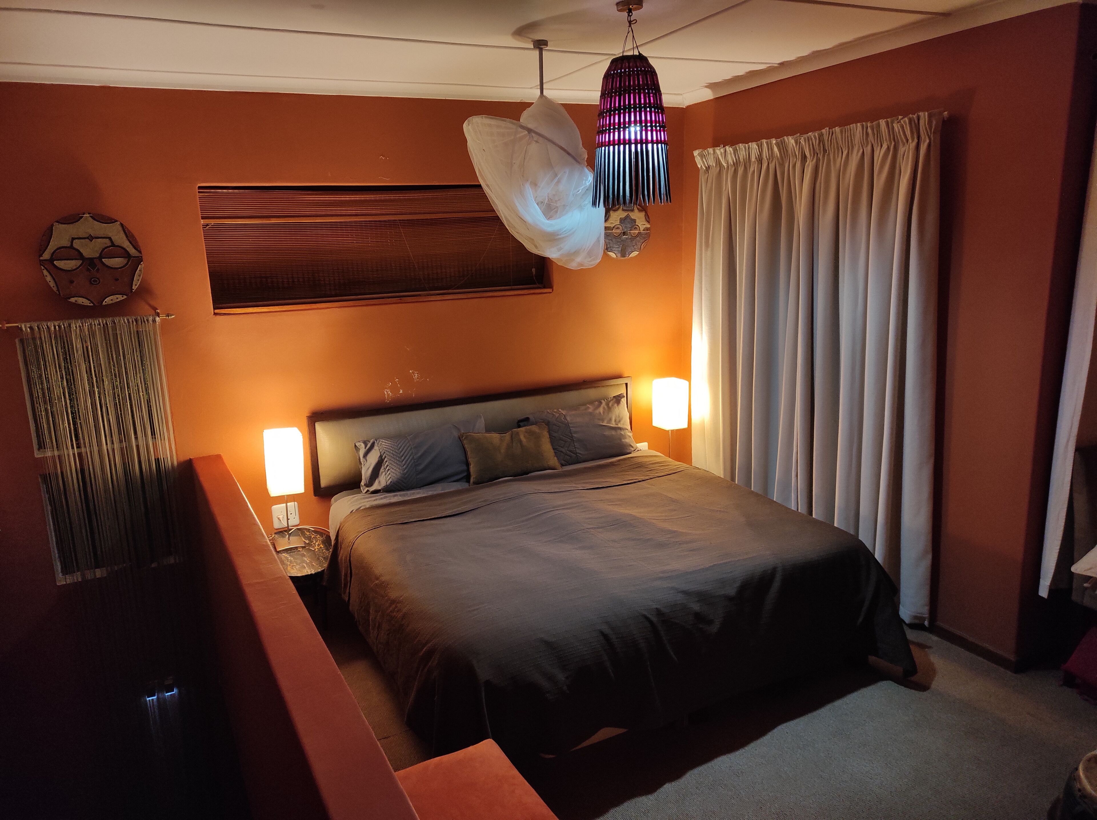A bedroom with a large bed, two bedside tables, a hanging light fixture, and a window with curtains.
