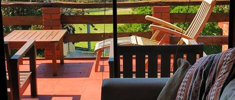 A balcony with a view of the beach and ocean, wooden furniture, and a sofa with a patterned pillow.