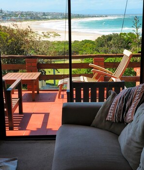 Un balcon avec vue sur la plage et l’océan, des meubles en bois et un canapé agrémenté d’un coussin à motifs.