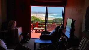Un salon doté d’une grande porte-fenêtre coulissante donnant sur un balcon avec vue sur la plage et l’océan.
