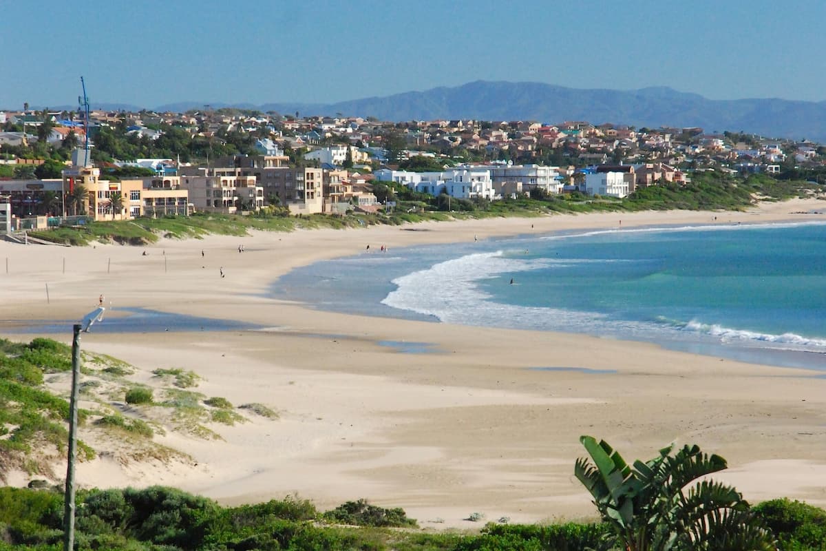 Eine Küstenstadt mit einem Sandstrand, blauem Himmel und Bergen in der Ferne.