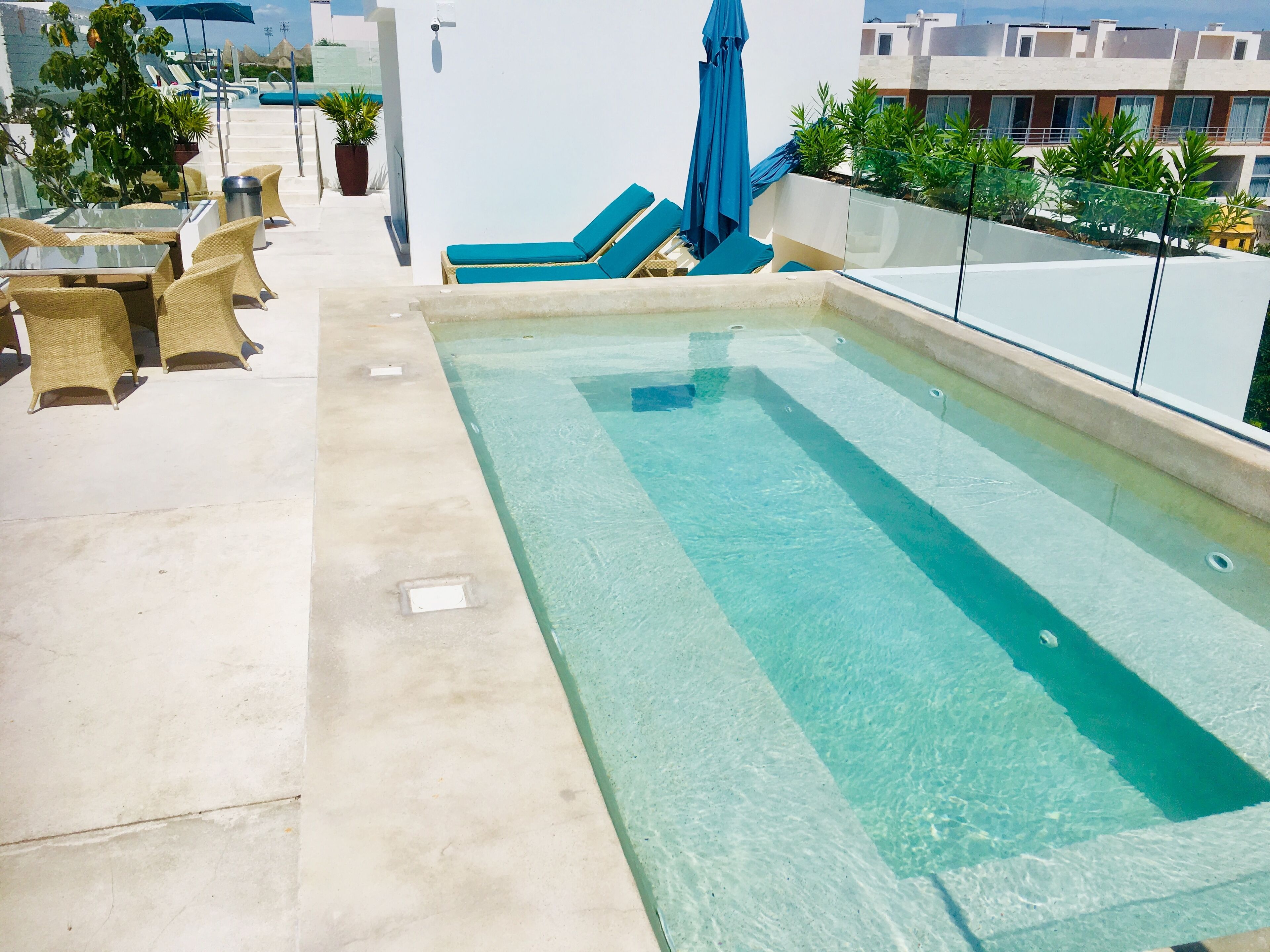 A rooftop pool with clear water, surrounded by lounge chairs and a table.