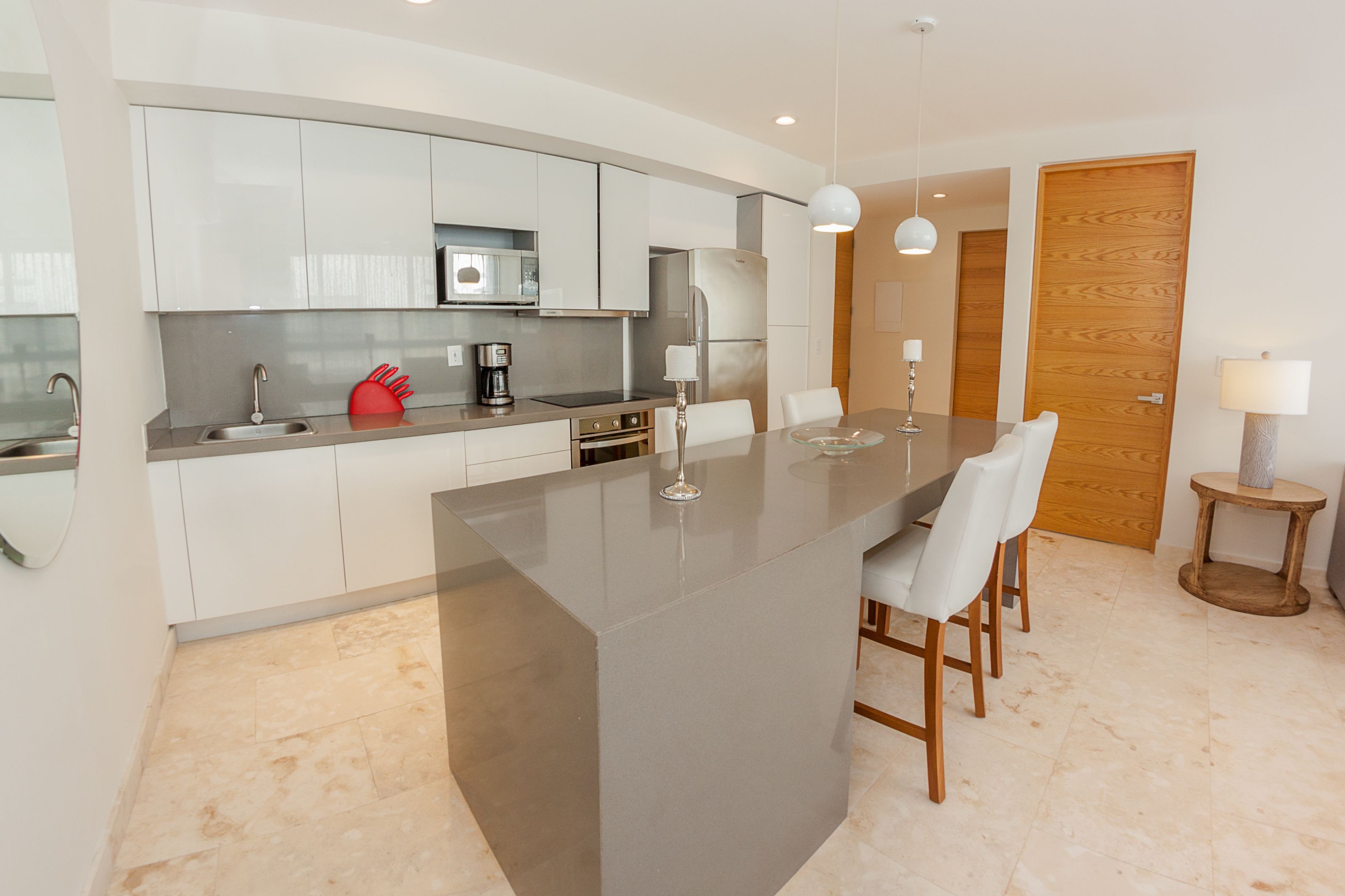 A modern kitchen with white cabinets, a central island, and a dining area with white chairs.