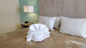 A neatly made bed with white pillows and a folded towel, a bedside table with a lamp, and a wall with a switch. - Anah Downtown DT 201B (Playa del Carmen)