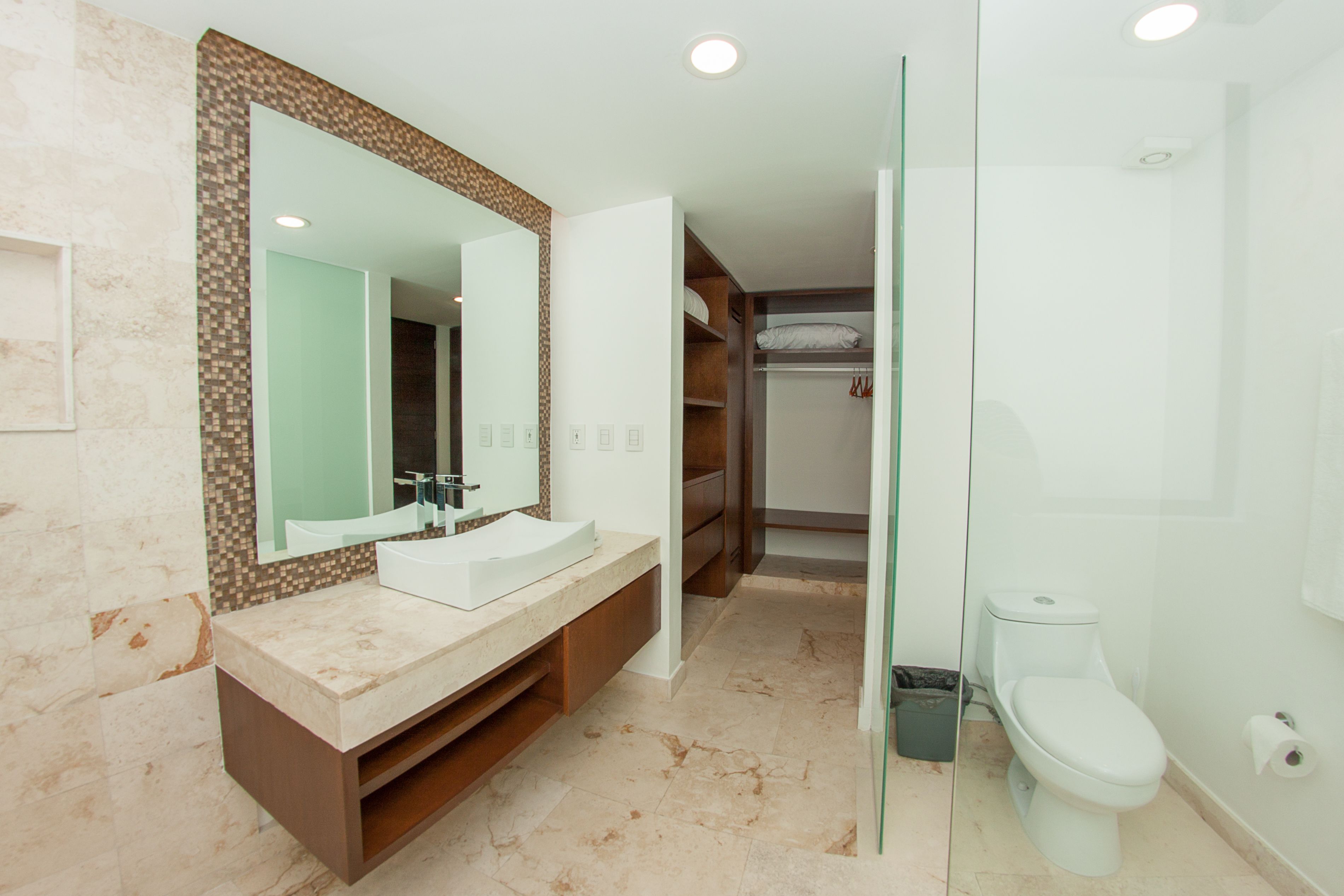 Une salle de bain moderne avec un meuble-lavabo en marbre, un grand miroir, une douche à l’italienne et un dressing.