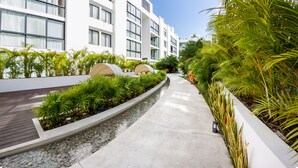 A modern hotel with a clean, white facade, a paved walkway, and lush greenery. - Anah Downtown DT 201B (Playa del Carmen)