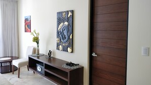 A modern living room with a dark wooden cabinet, a wall-mounted artwork, a dining area with a round table and chairs, and a large wooden door. - Anah Downtown DT 201B (Playa del Carmen)
