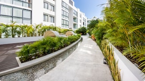 Een modern hotel met een strak, wit gevel, een verhard pad en weelderige begroeiing.