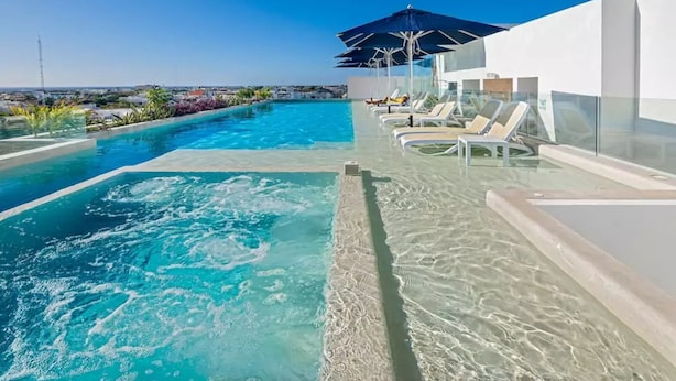 Een dakzwembad in oneindigheid met helderblauw water, omringd door ligbedden en parasols, met uitzicht op een stadsgezicht.
