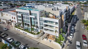 Un hôtel moderne à plusieurs étages, doté d’une piscine sur le toit et offrant une vue sur la rue, où l’on peut voir des voitures garées.