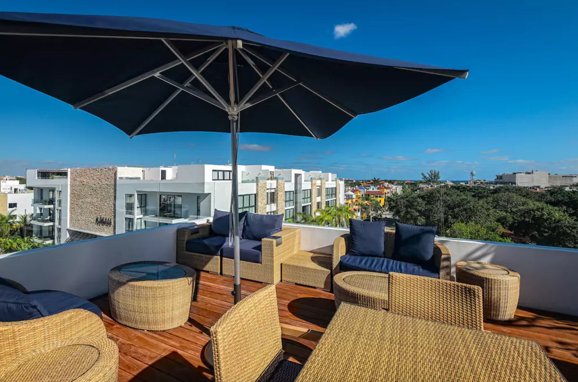 Een terras op het dak met rieten meubilair, een grote parasol en uitzicht op moderne gebouwen.