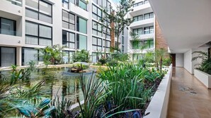 Un bâtiment moderne doté d’une cour intérieure où se trouve un petit étang, le tout entouré d’une végétation luxuriante et de plantes.