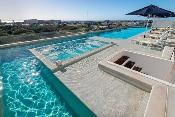 Una piscina infinita en la azotea con agua cristalina, una tumbona y vistas de la ciudad.