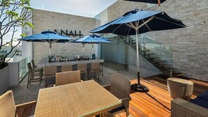 Un espace extérieur aménagé en terrasse, avec des meubles en osier, des parasols bleus et un bar.