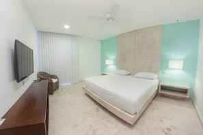 A modern hotel room with a large bed, a flat-screen TV, a ceiling fan, and a wicker chair.