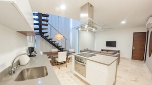 A modern kitchen with a central island, a dining area, and a staircase leading to an upper level. - Anah Downtown DT 408 (Playa del Carmen)
