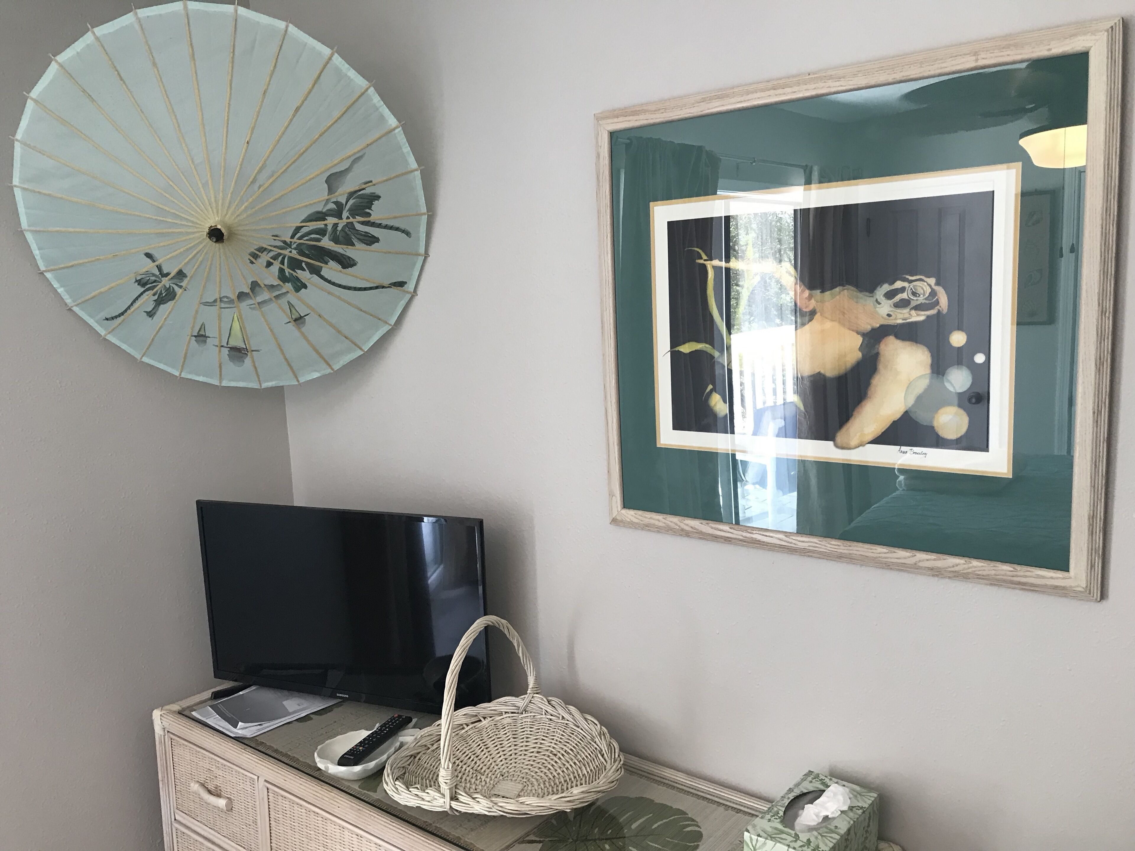 Une pièce comprenant une télévision, un tableau encadré, un éventail décoratif et un panier en osier.