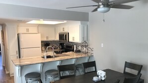 Una cocina moderna con armarios blancos, encimera de madera y comedor con mesa y sillas de madera oscura.