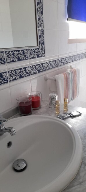 A bathroom with a white sink, two glass candle holders with red candles, and two bottles of liquid. - Elodie's Country House (Grandola)