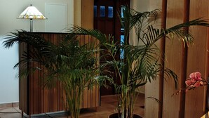 A spacious indoor area with tiled flooring, potted plants, a glass table with a basket, and wooden paneling on the walls.
