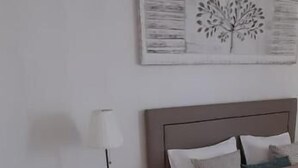 A bedroom with a bed, a nightstand with a lamp, and a wall-mounted artwork.