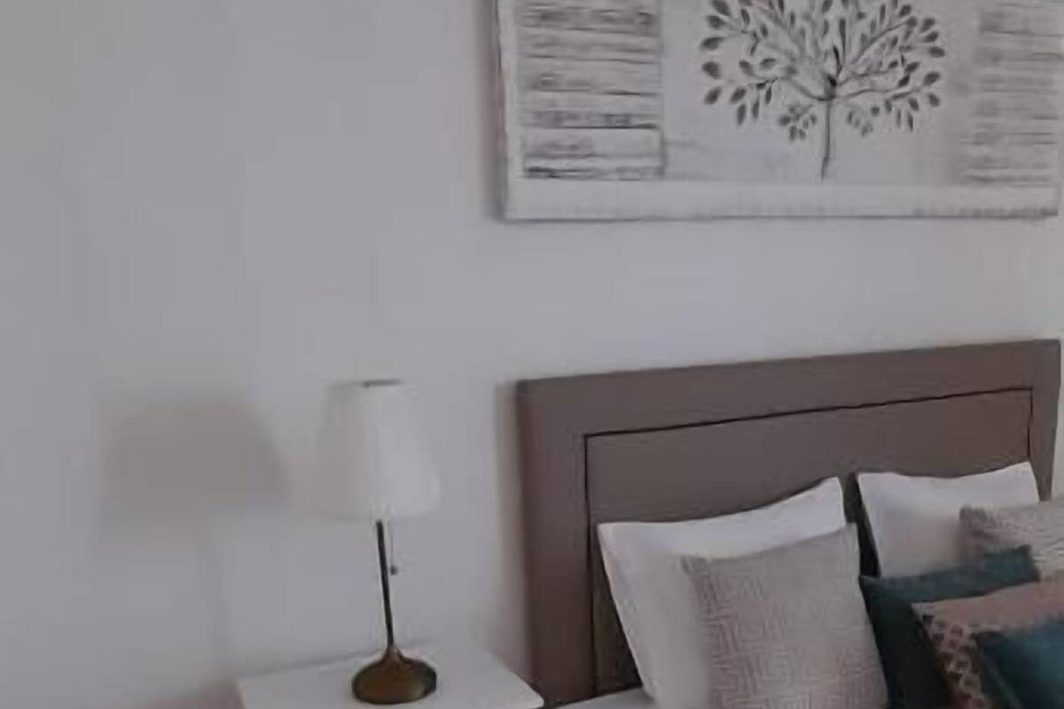 Ein Schlafzimmer mit einem Bett, einem Nachttisch mit Lampe und einem Wandbild.