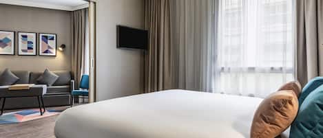 Una habitación de hotel moderna con una cama grande, un sofá, un televisor y una ventana con cortinas.