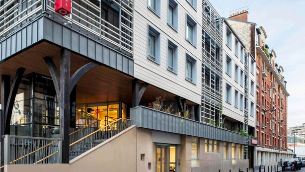 Un hotel moderno con un llamativo letrero rojo, un vestíbulo cubierto y una escalera que conduce a la recepción.