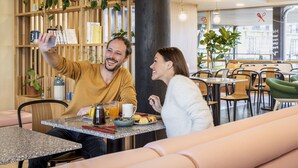 Una pareja se toma un selfie en una mesa de desayuno con una cafetera, jugo de naranja y pasteles.