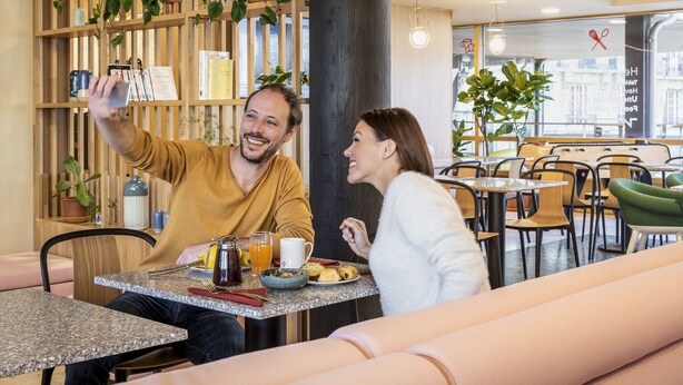 A couple taking a selfie at a breakfast table with a coffee pot, orange juice, and pastries. - Aparthotel Adagio Paris Nation (Paris)
