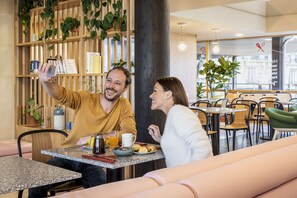 Una pareja se toma un selfie en una mesa de desayuno con una cafetera, jugo de naranja y pasteles.