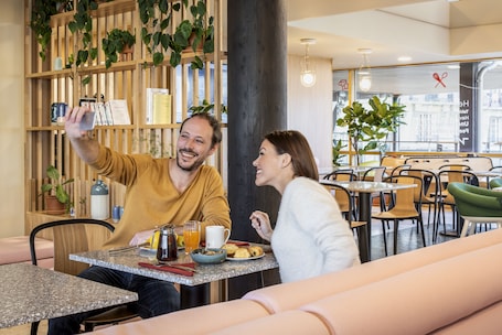 A couple taking a selfie at a breakfast table with a coffee pot, orange juice, and pastries.