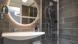 Un baño moderno con un lavamanos grande, un espejo, una ducha y un perchero para toallas.