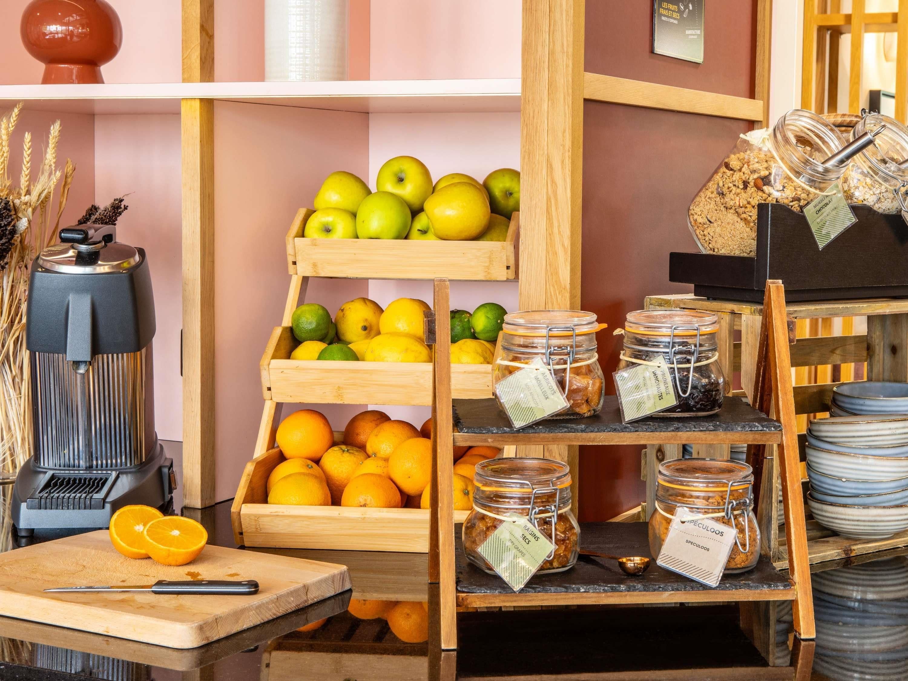Une cuisine avec des étagères en bois où sont disposés des fruits, une machine à café et des pots de confitures.