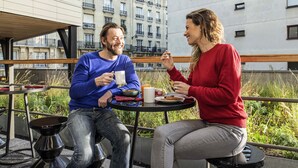 Two people seated at an outdoor table with a cityscape view, a metal chair, and a small table with a cup and a plate. - Aparthotel Adagio Paris Nation (Paris)