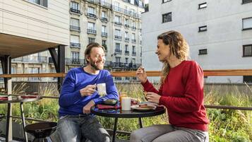 Due persone sedute a un tavolo all'aperto con vista sulla città, una sedia in metallo e un tavolino con una tazza e un piatto.