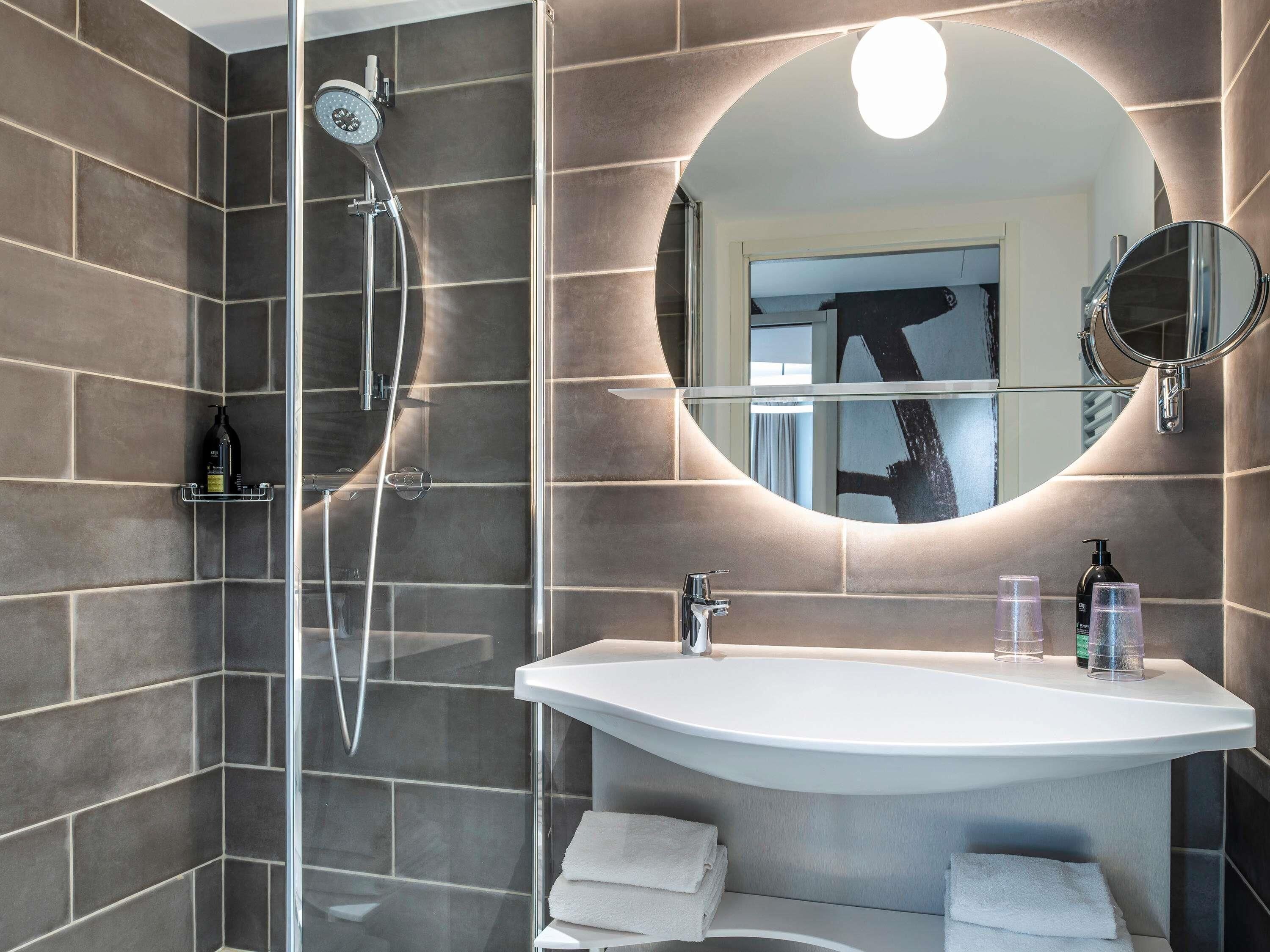 Un baño moderno con ducha envuelta en vidrio, un lavamanos blanco y un espejo grande.